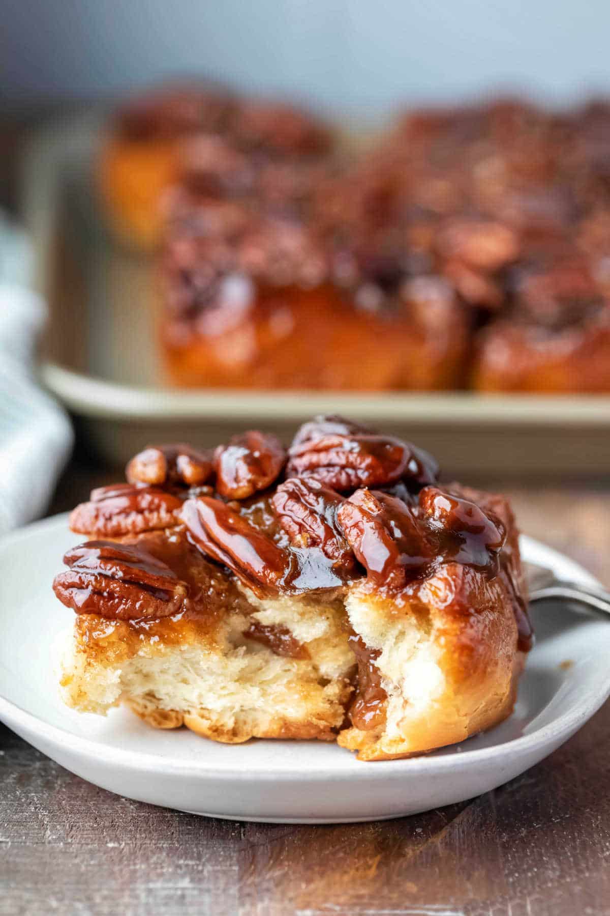 Maple sticky bun on a white plate with a piece missing from the front. 