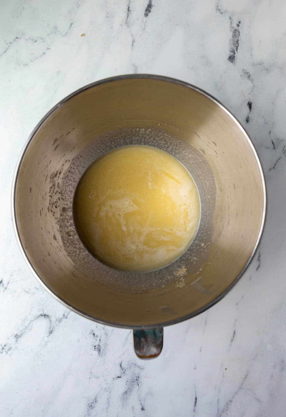 Melted butter and milk and yeast  in a silver mixing bowl. 
