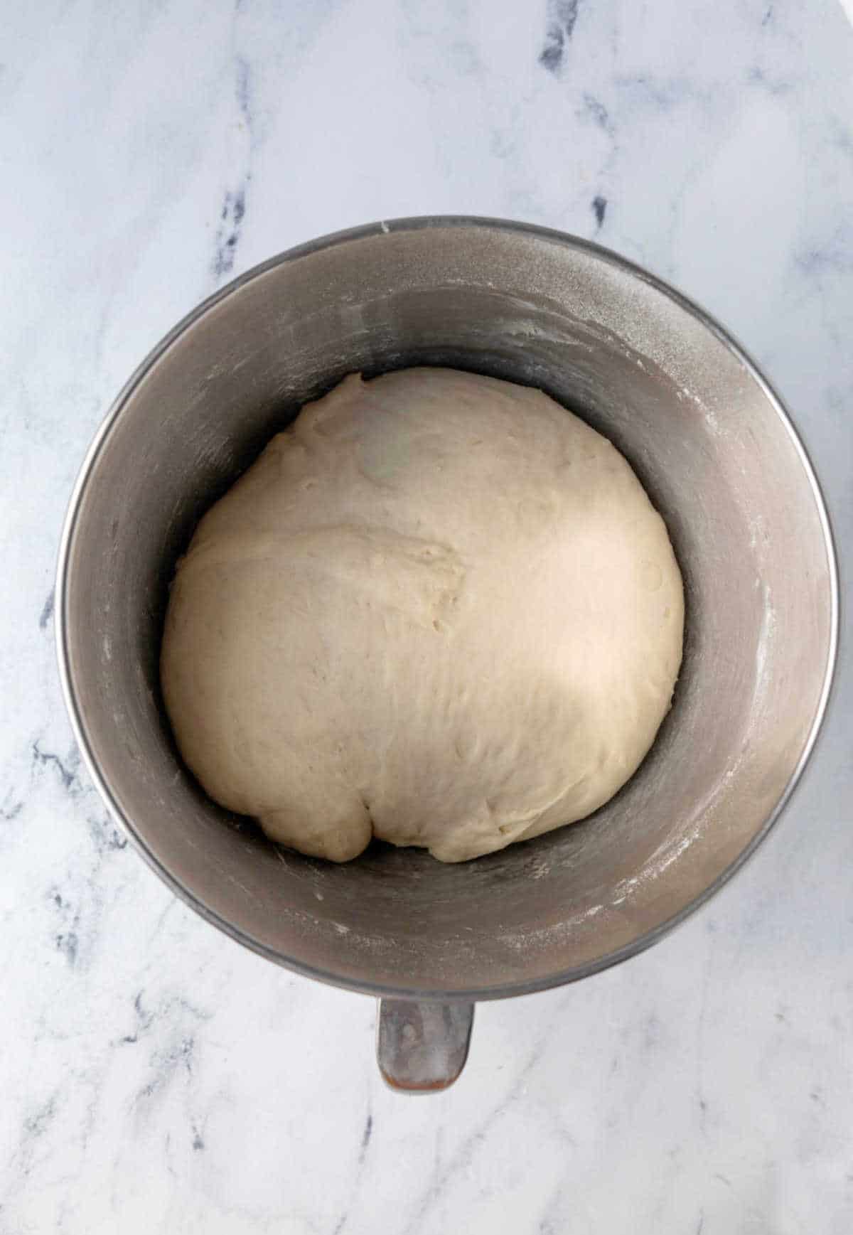 Risen sticky bun dough in a silver mixing bowl.