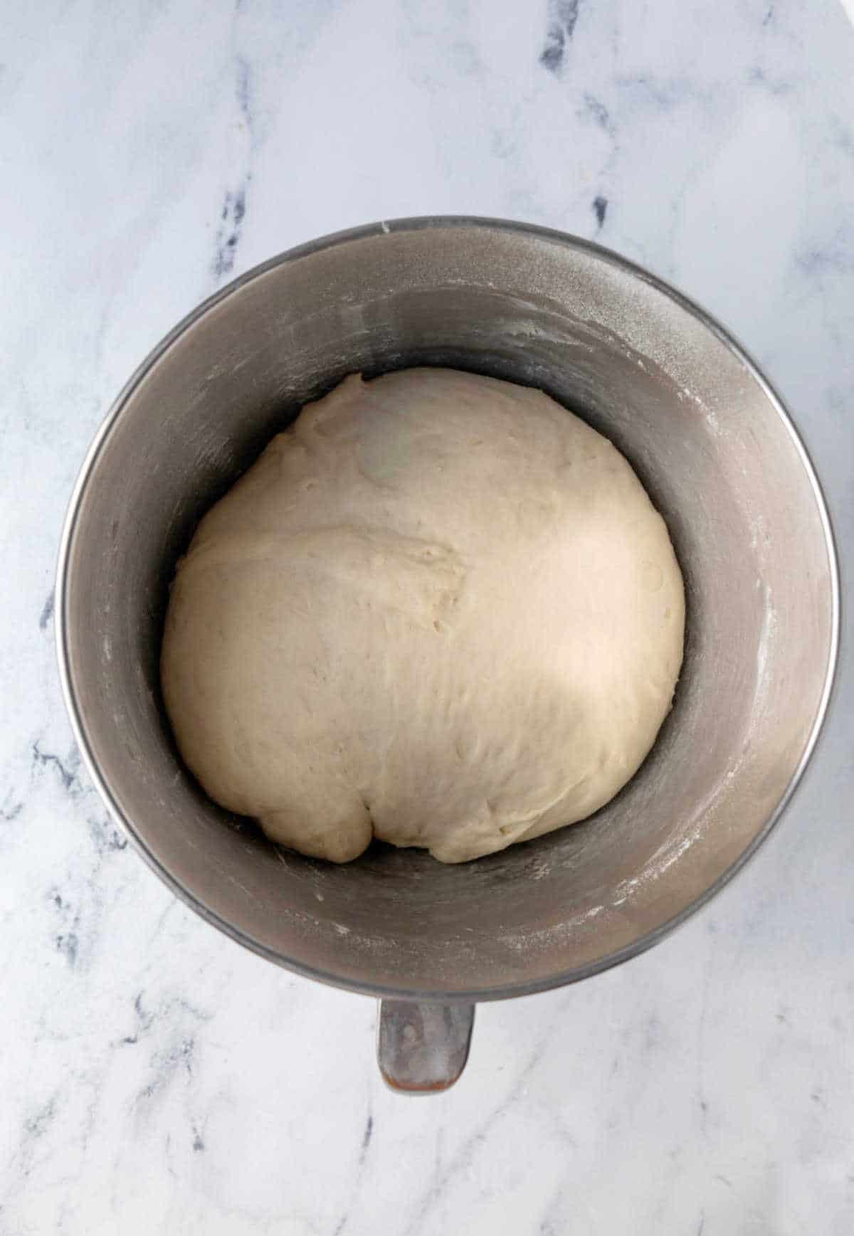 Risen sticky bun dough in a silver mixing bowl. 