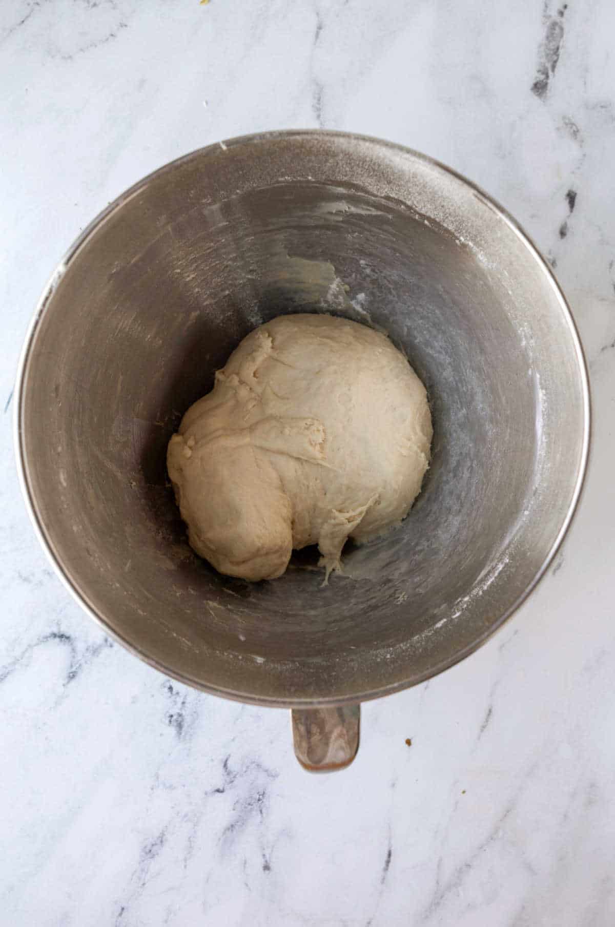 Kneaded sticky bun dough in a silver mixing bowl. 