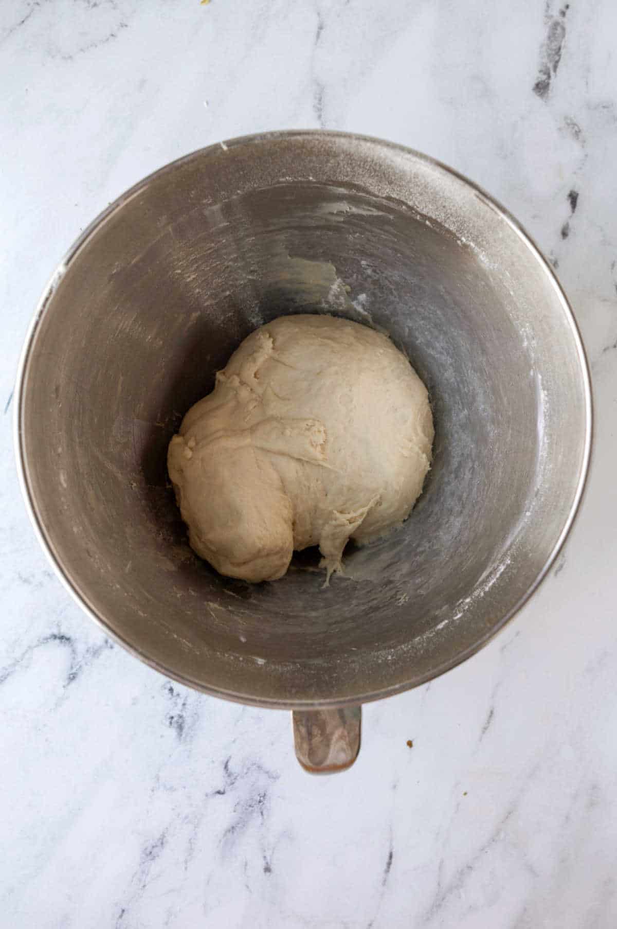 Kneaded sticky bun dough in a silver mixing bowl.