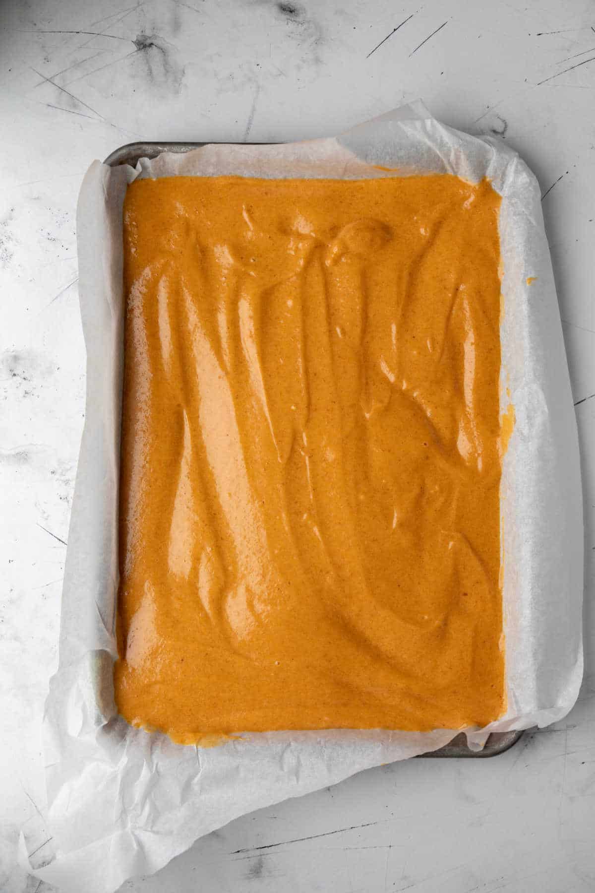 Pumpkin cake batter in a jelly roll pan.