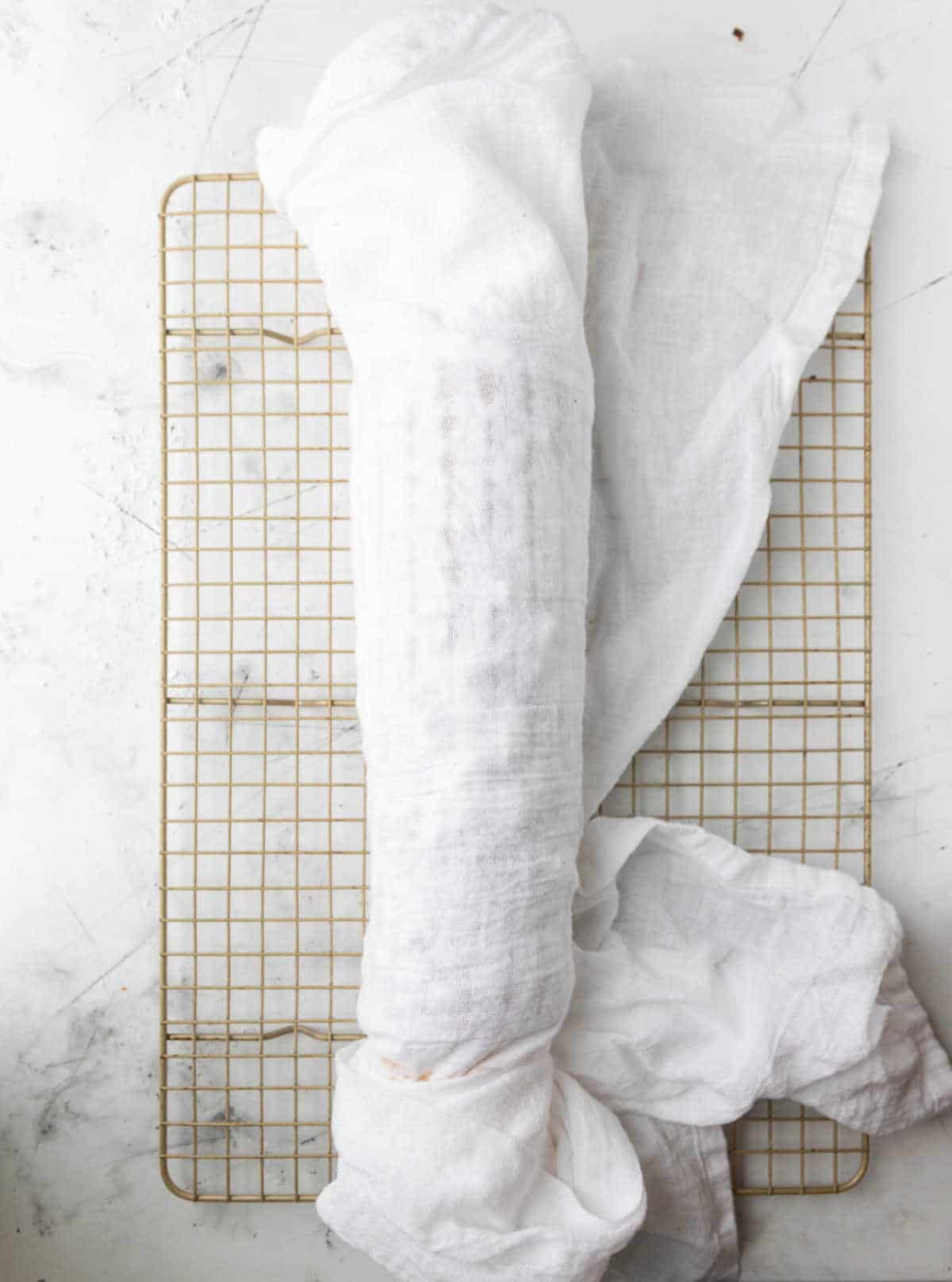 Cake wrapped in a flour sack towel on a wire cooling rack.