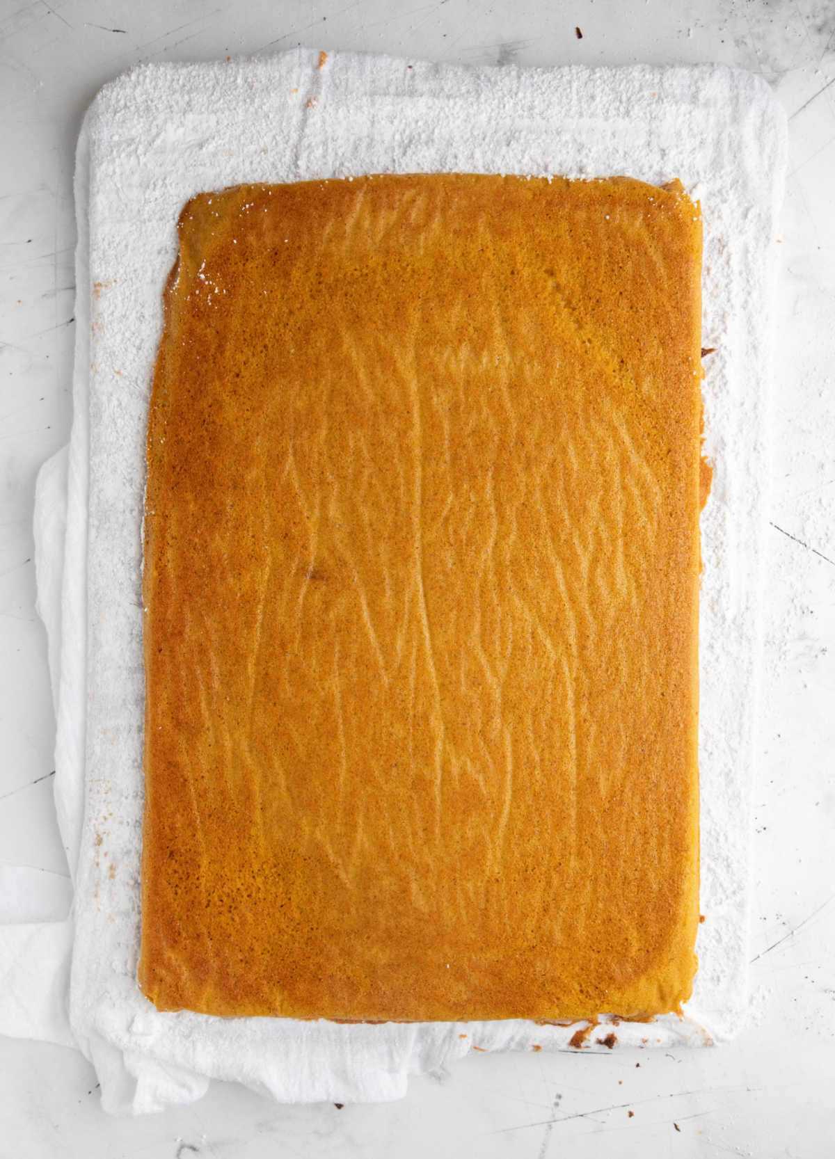 Cooled pumpkin roll unrolled on a flour sack towel. 