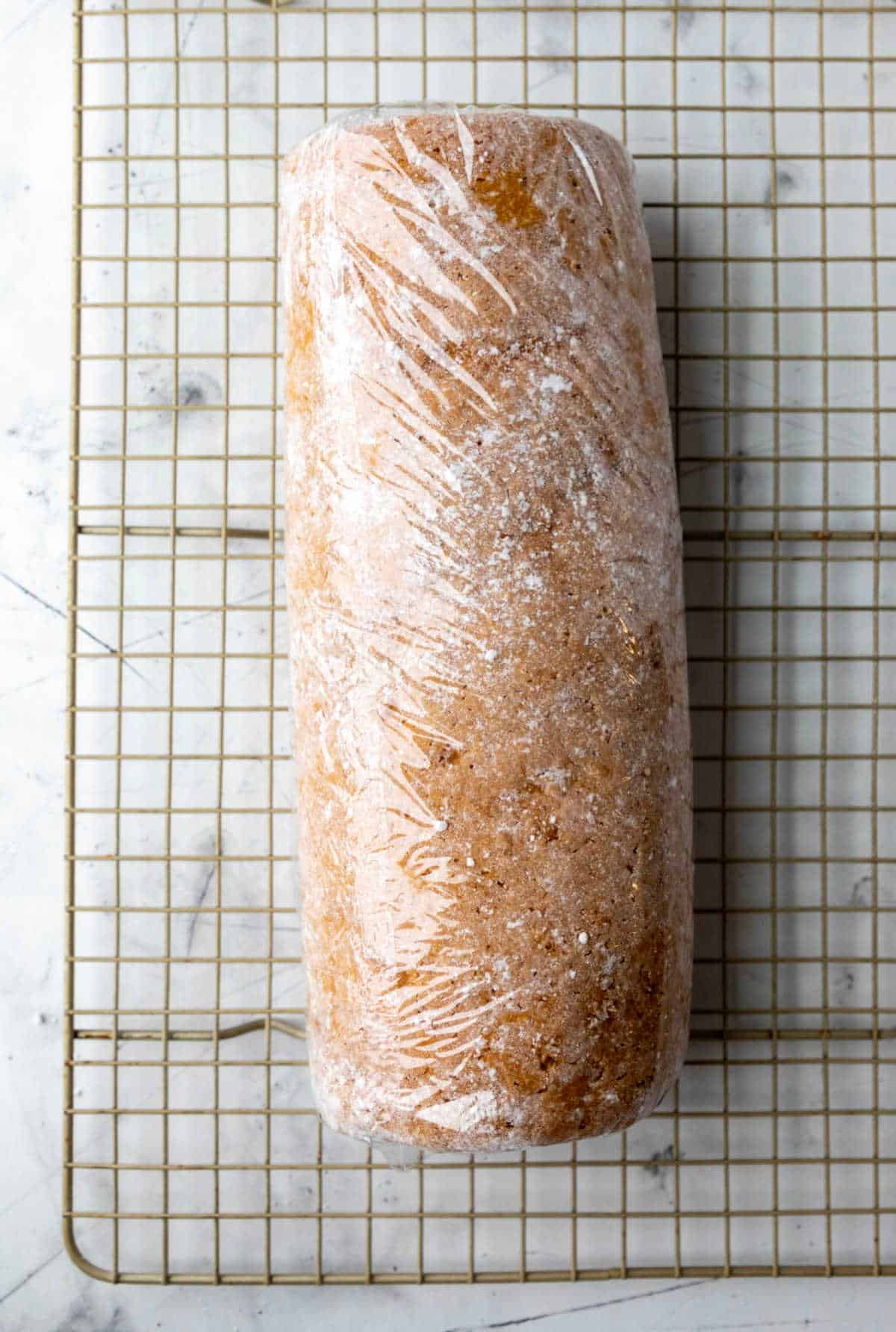 Pumpkin roll cake wrapped in plastic wrap on a wire cooling rack. 