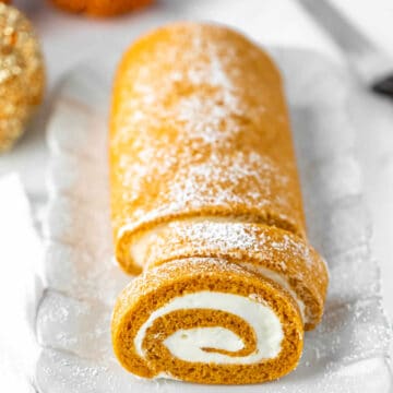 Pumpkin roll with two slices cut on a white platter.