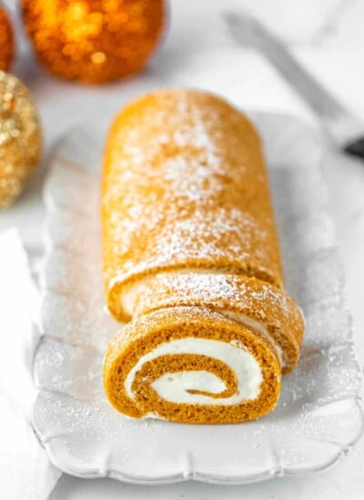 Pumpkin roll with two slices cut on a white platter.