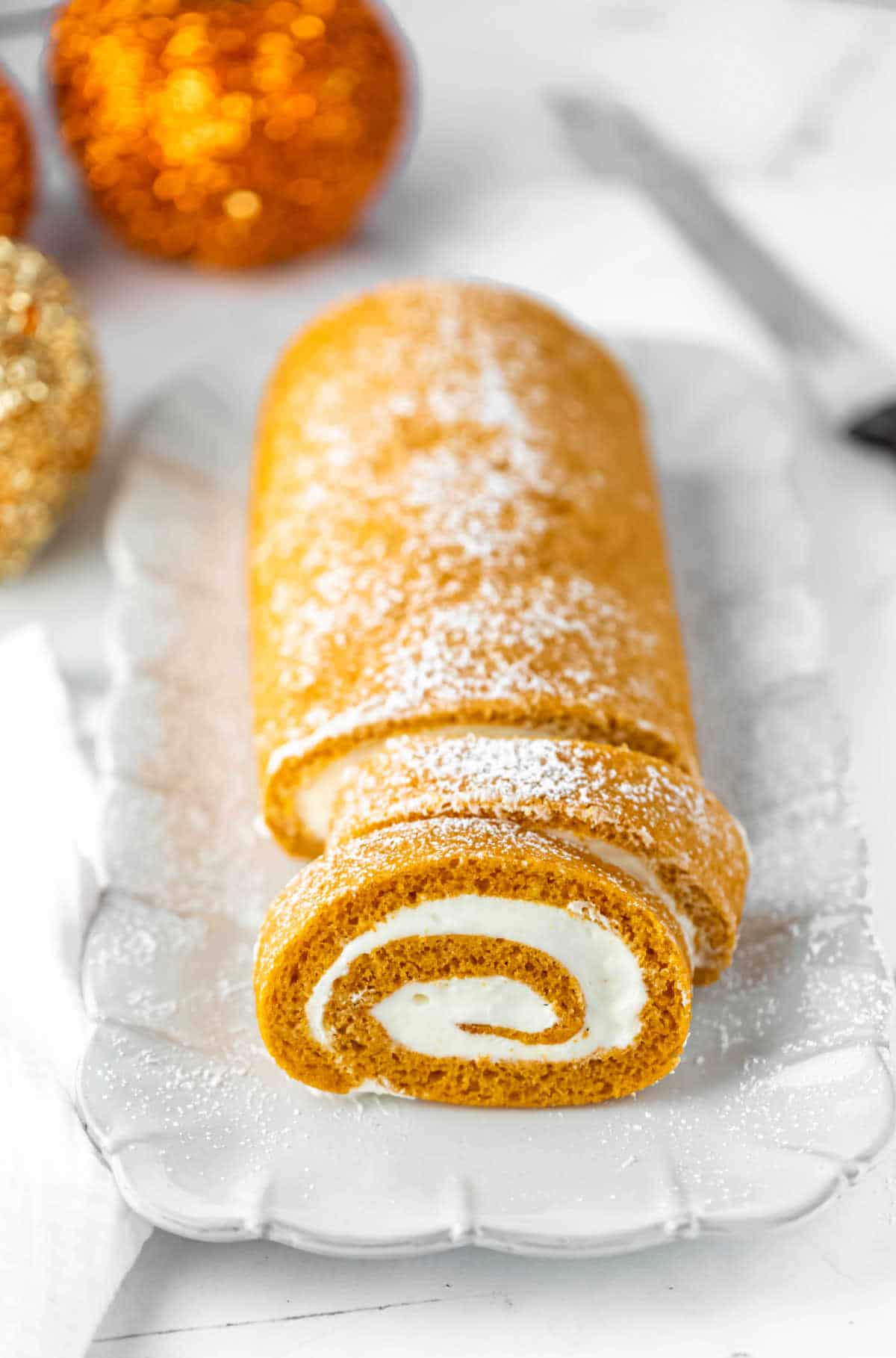 Pumpkin roll with two slices cut on a white platter.