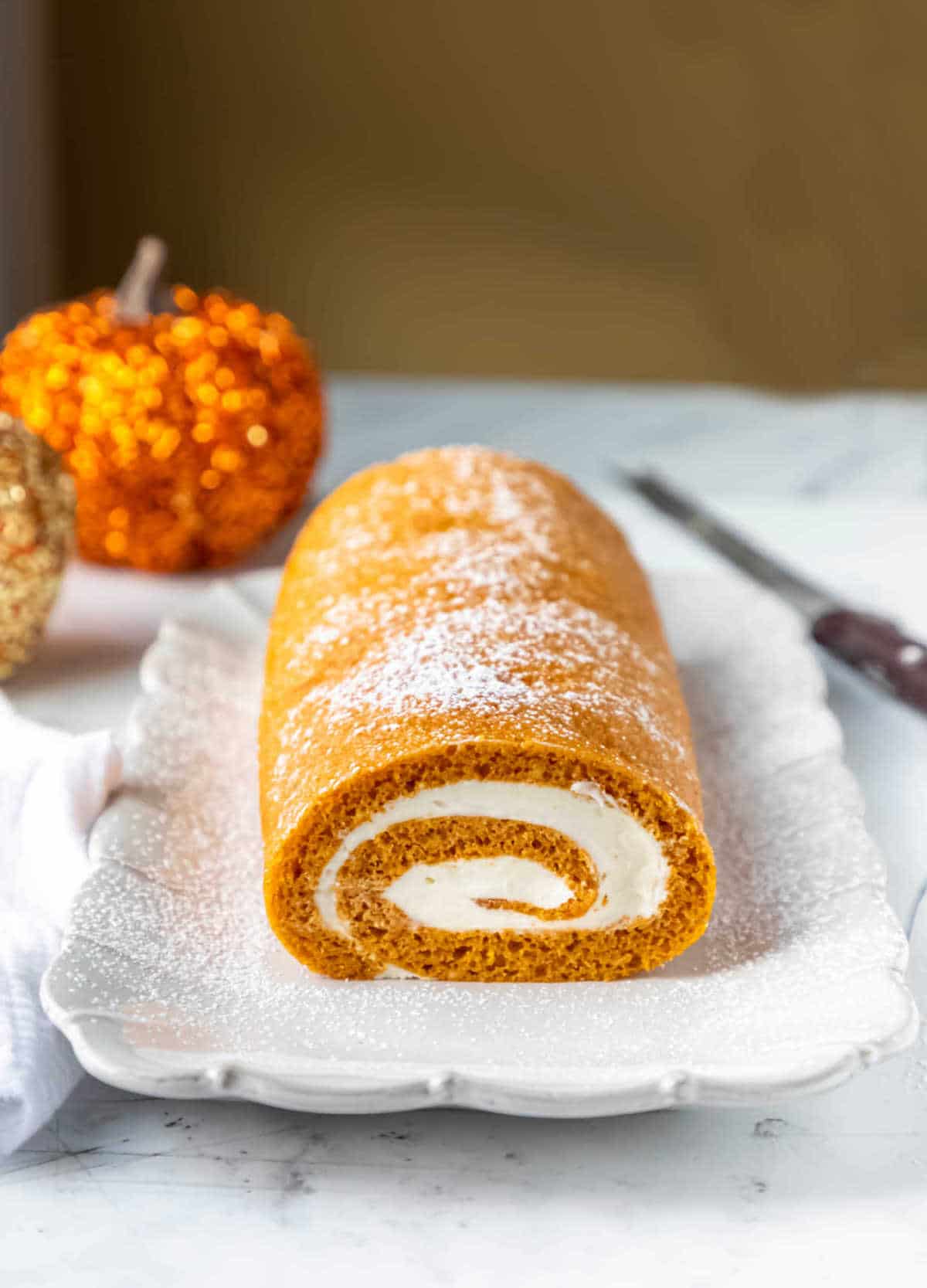 Pumpkin roll on a white platter next to a serrated knife. 