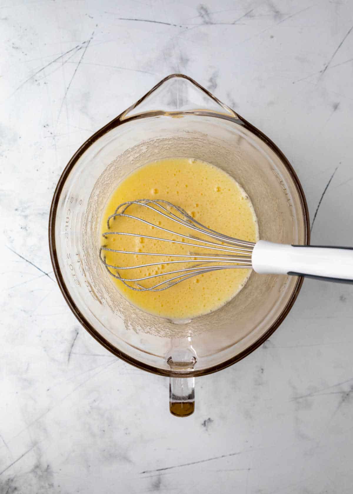 Beaten eggs and sugar in a glass mixing bowl. 