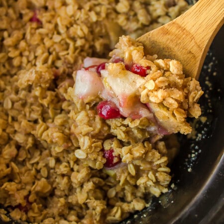 Wooden spoon scooping up cranberry apple crisp from a slow cooker.