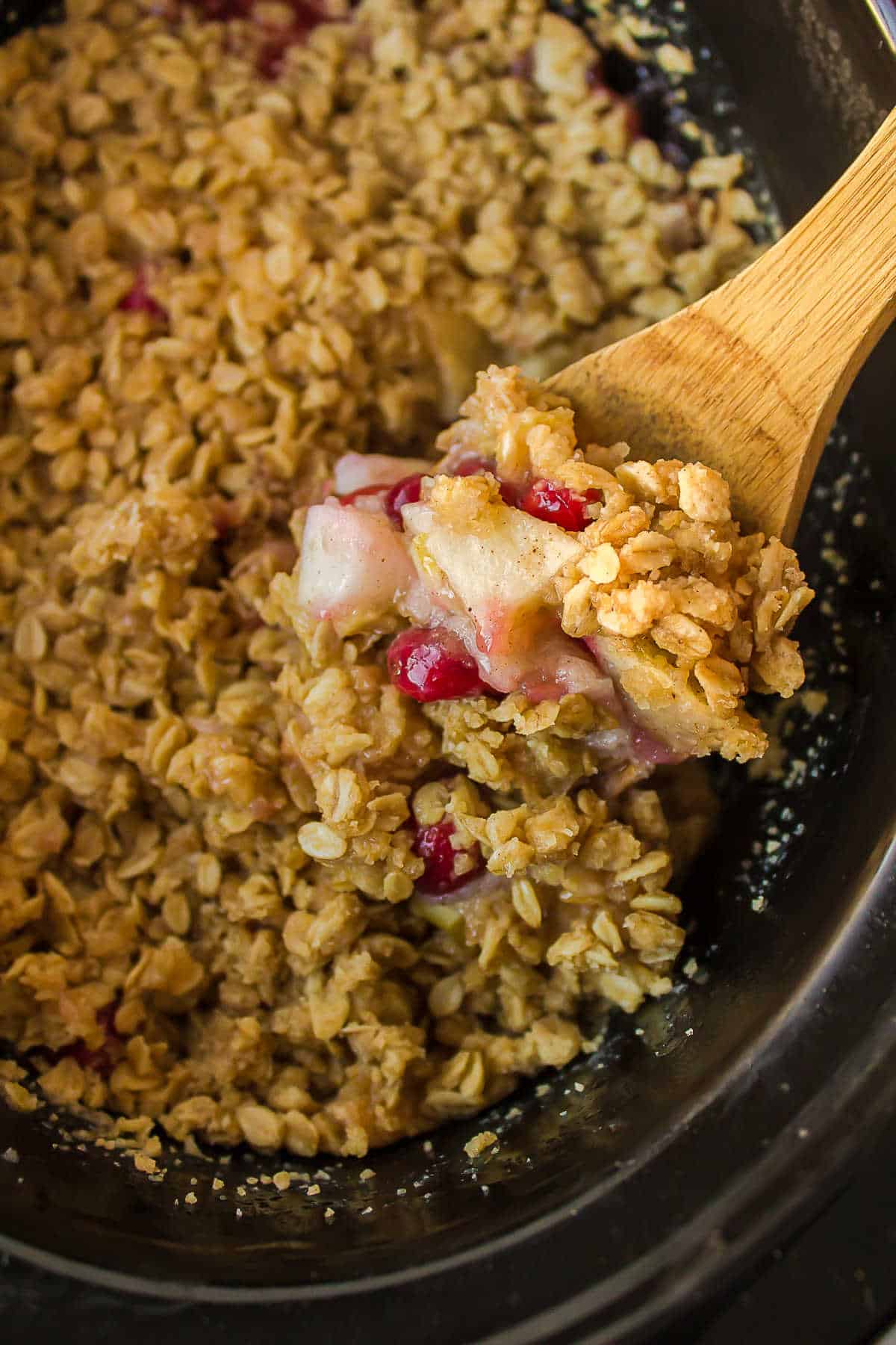 Wooden spoon scooping up cranberry apple crisp from a slow cooker. 