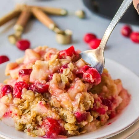 A plate of cranberry apple crisp with cranberries around it.