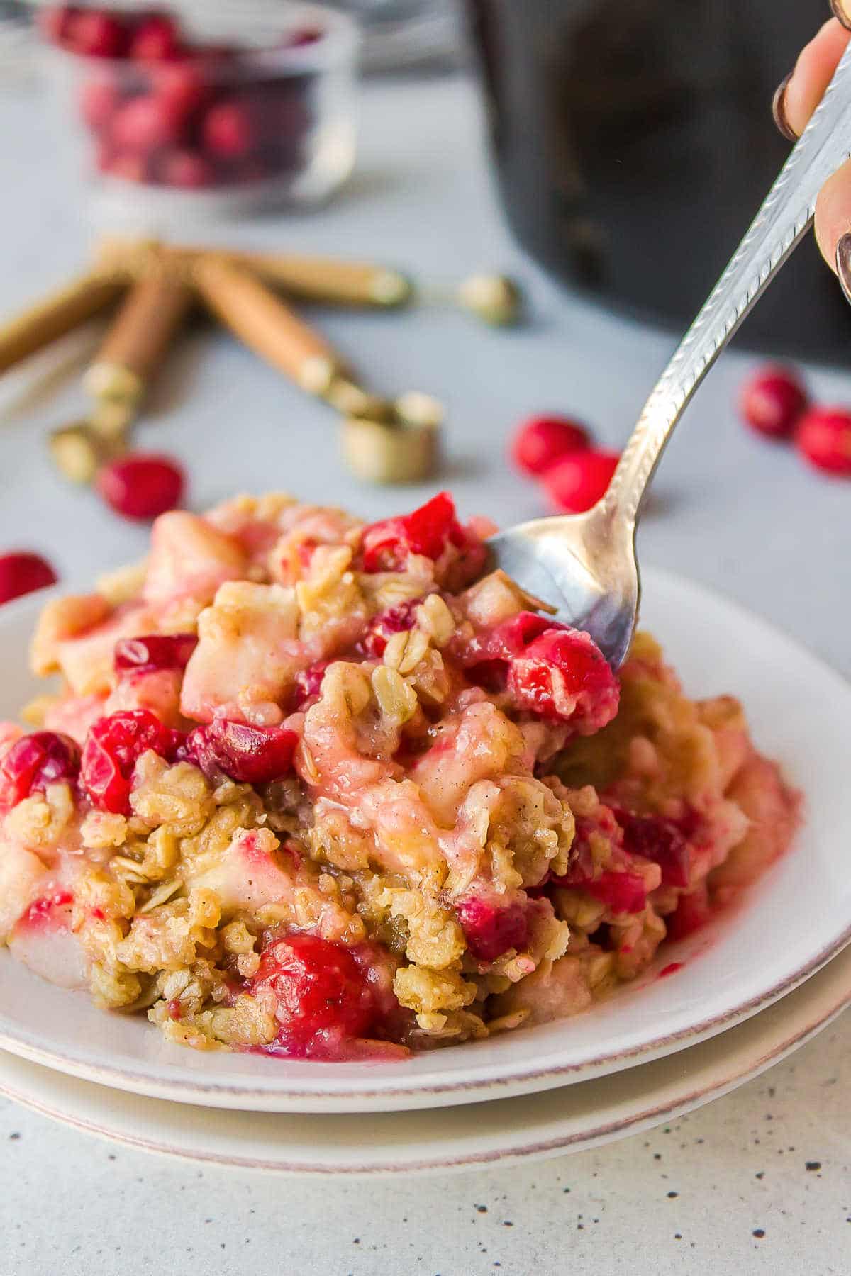 A plate of cranberry apple crisp with cranberries around it. 