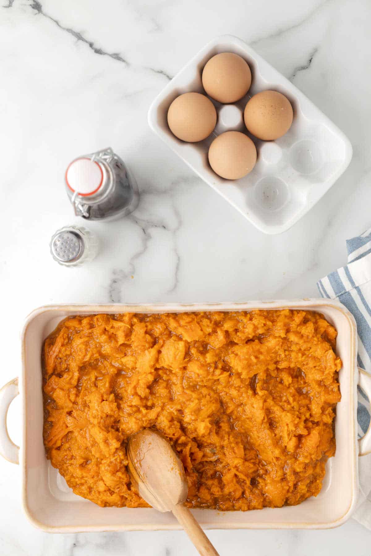 Wooden spoon spreading mashed sweet potato in a casserole dish.