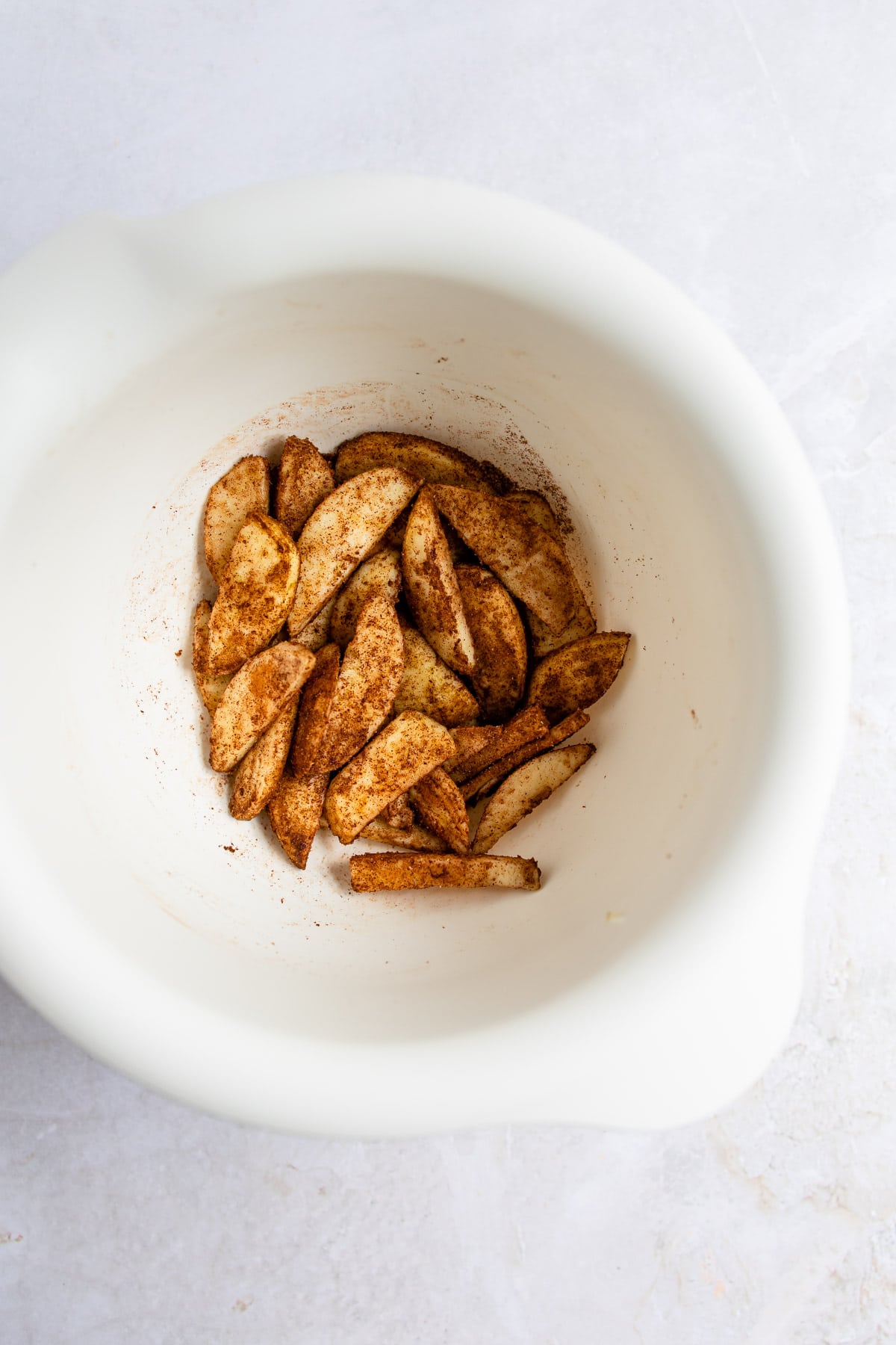 Apple slices coated with spices in a white mixing bowl.
