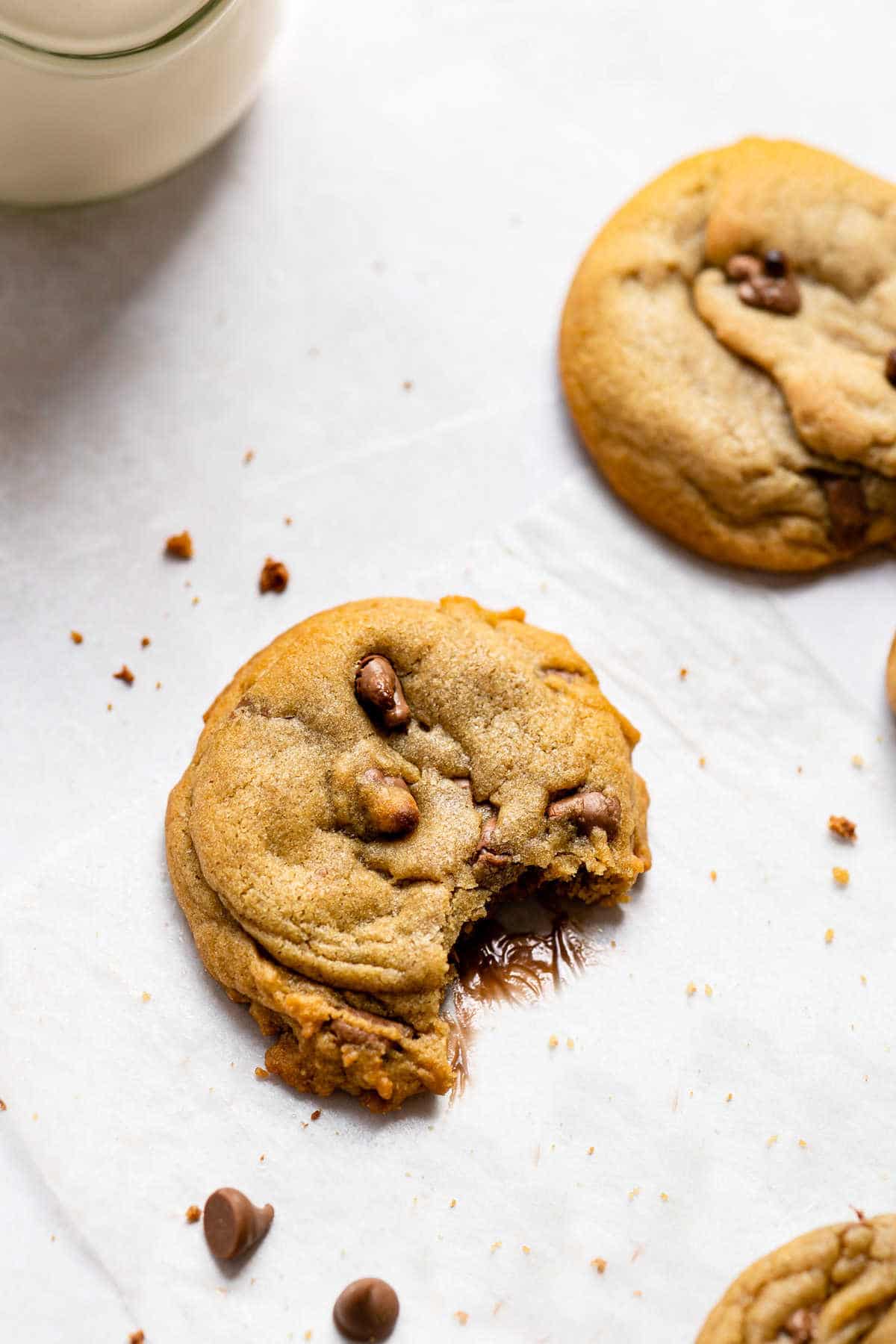 Two bakery style chocolate chip cookies next to a glass of milk. 