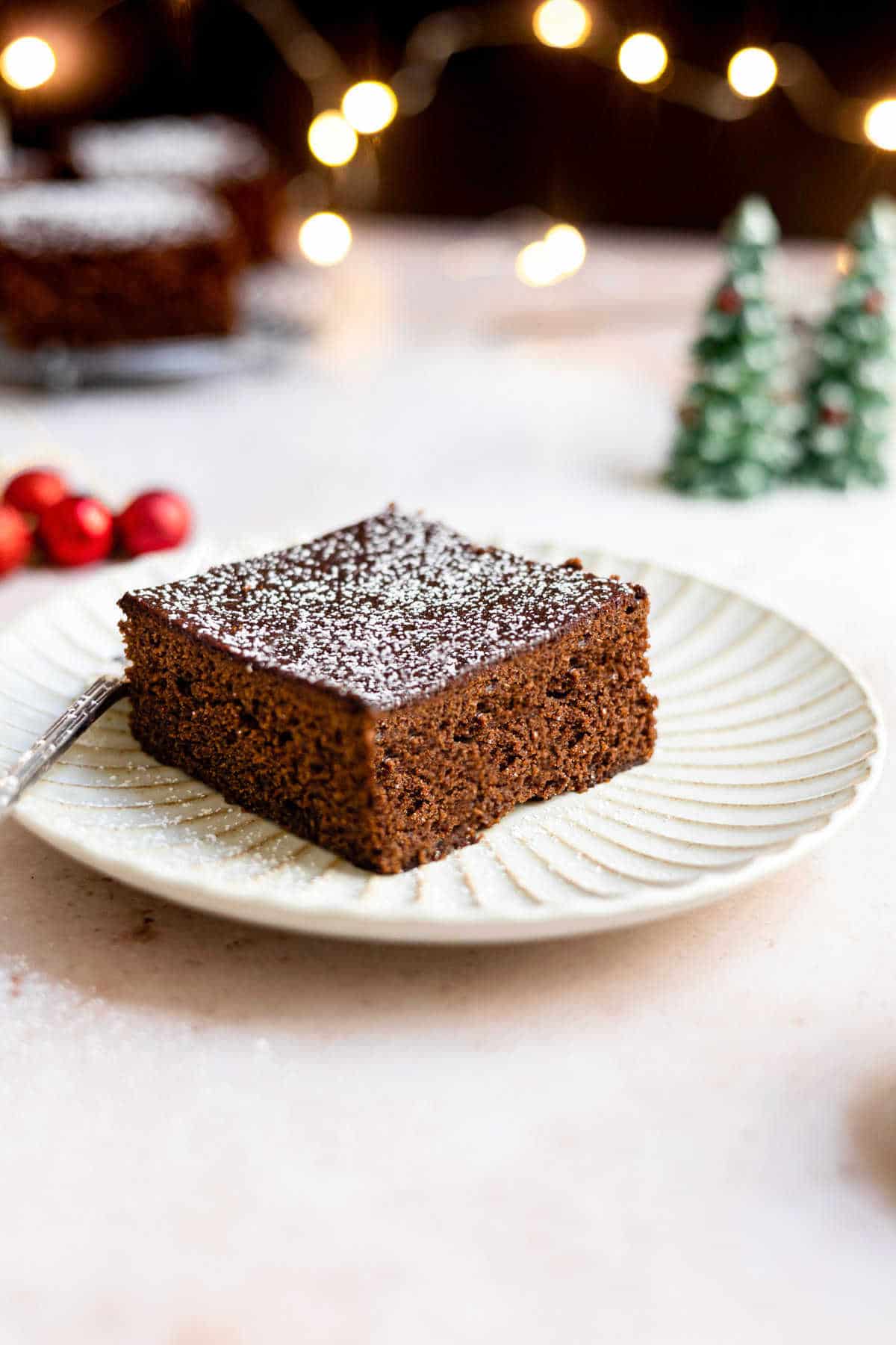 Piece of gingerbread on a white plate next to Christmas decorations.