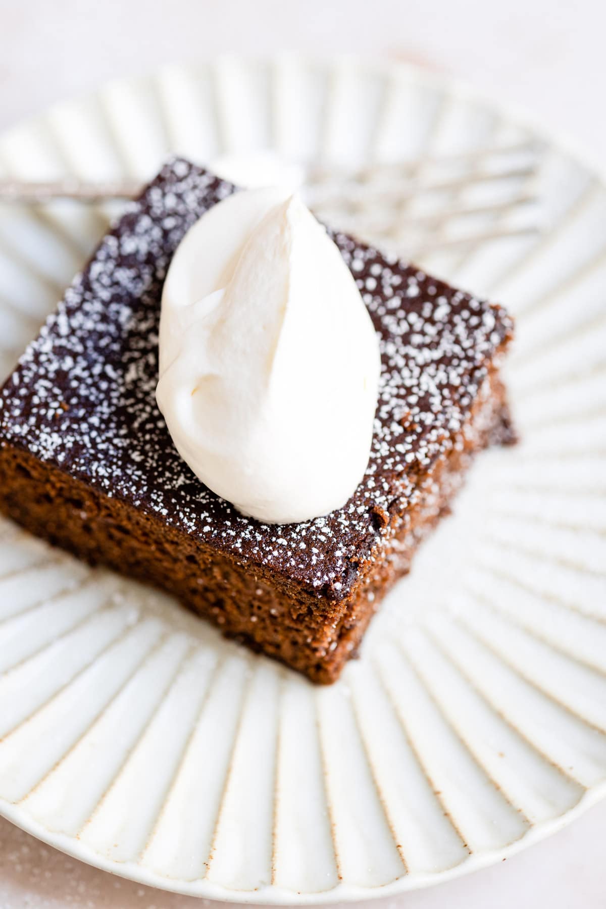 Close up photo of a piece of gingerbread topped with a dollop of whipped cream.