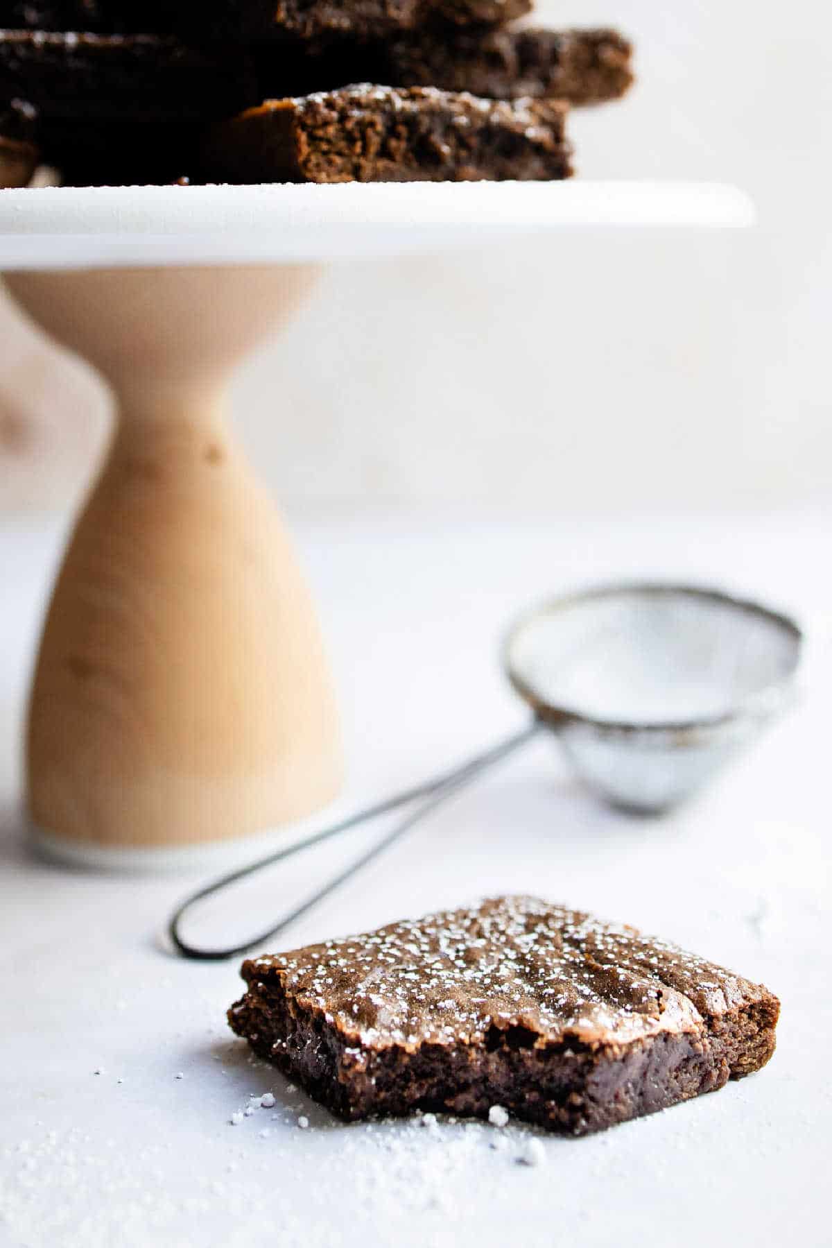 A gingerbread brownie next to a cake stand with a stack of brownies. 