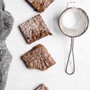 Four gingerbread brownies in a row next to a powdered sugar sifter.