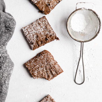 Four gingerbread brownies in a row next to a powdered sugar sifter.