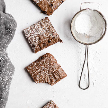 Four gingerbread brownies in a row next to a powdered sugar sifter.