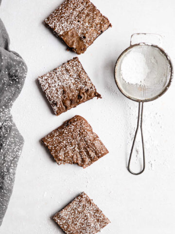 Four gingerbread brownies in a row next to a powdered sugar sifter.
