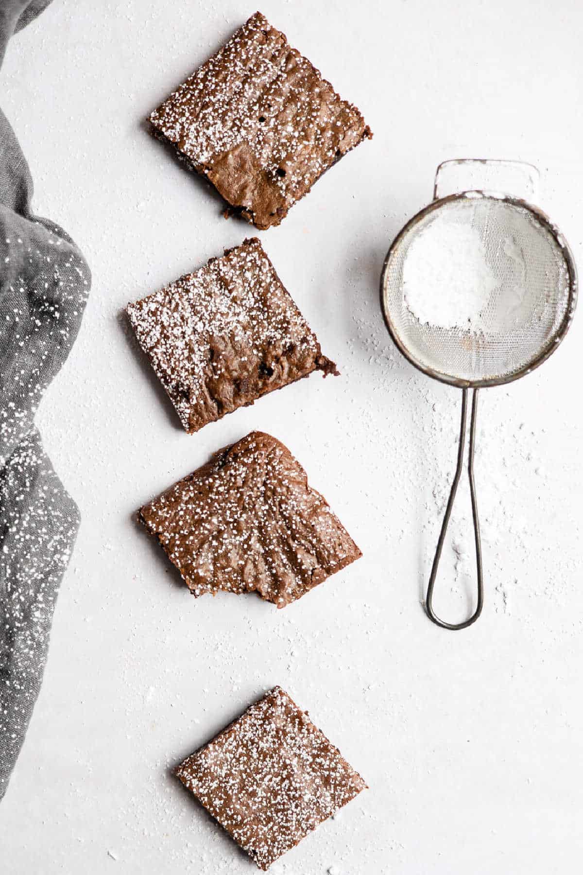 Four gingerbread brownies in a row next to a powdered sugar sifter.