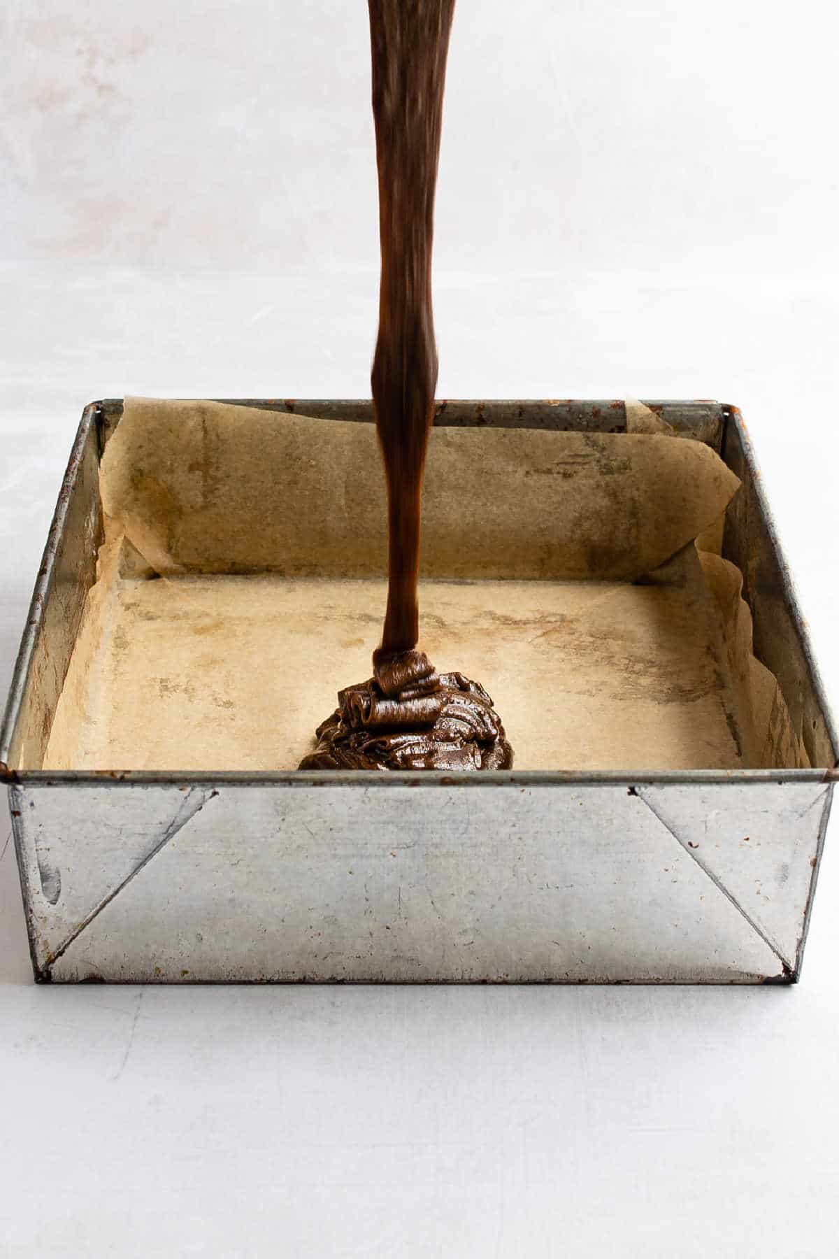 Gingerbread brownie batter pouring into a metal baking pan. 