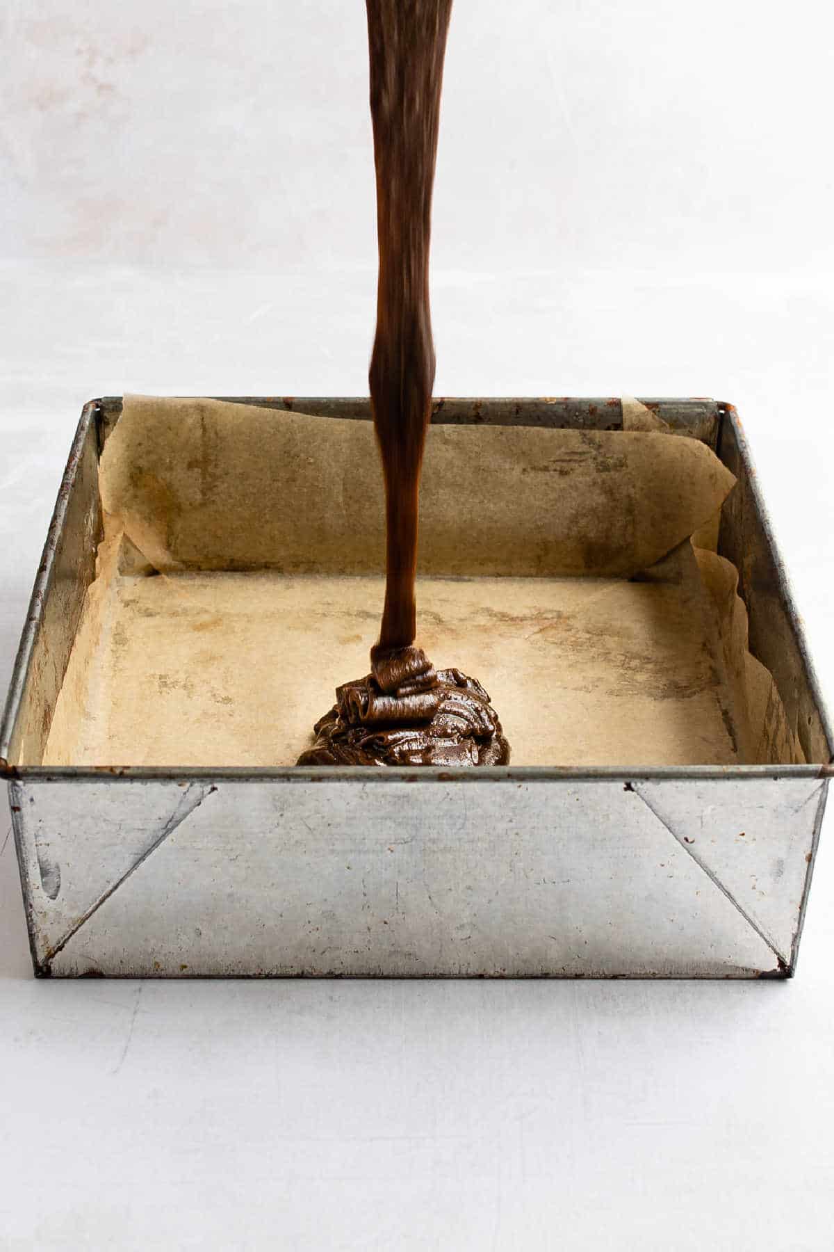 Gingerbread brownie batter pouring into a metal baking pan.