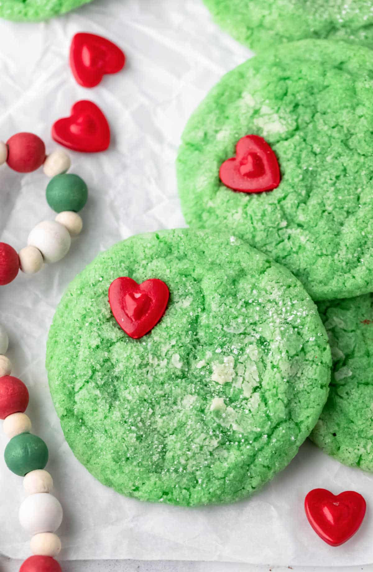 Close up photo of a Grinch cookie next to a beaded Christmas garland.