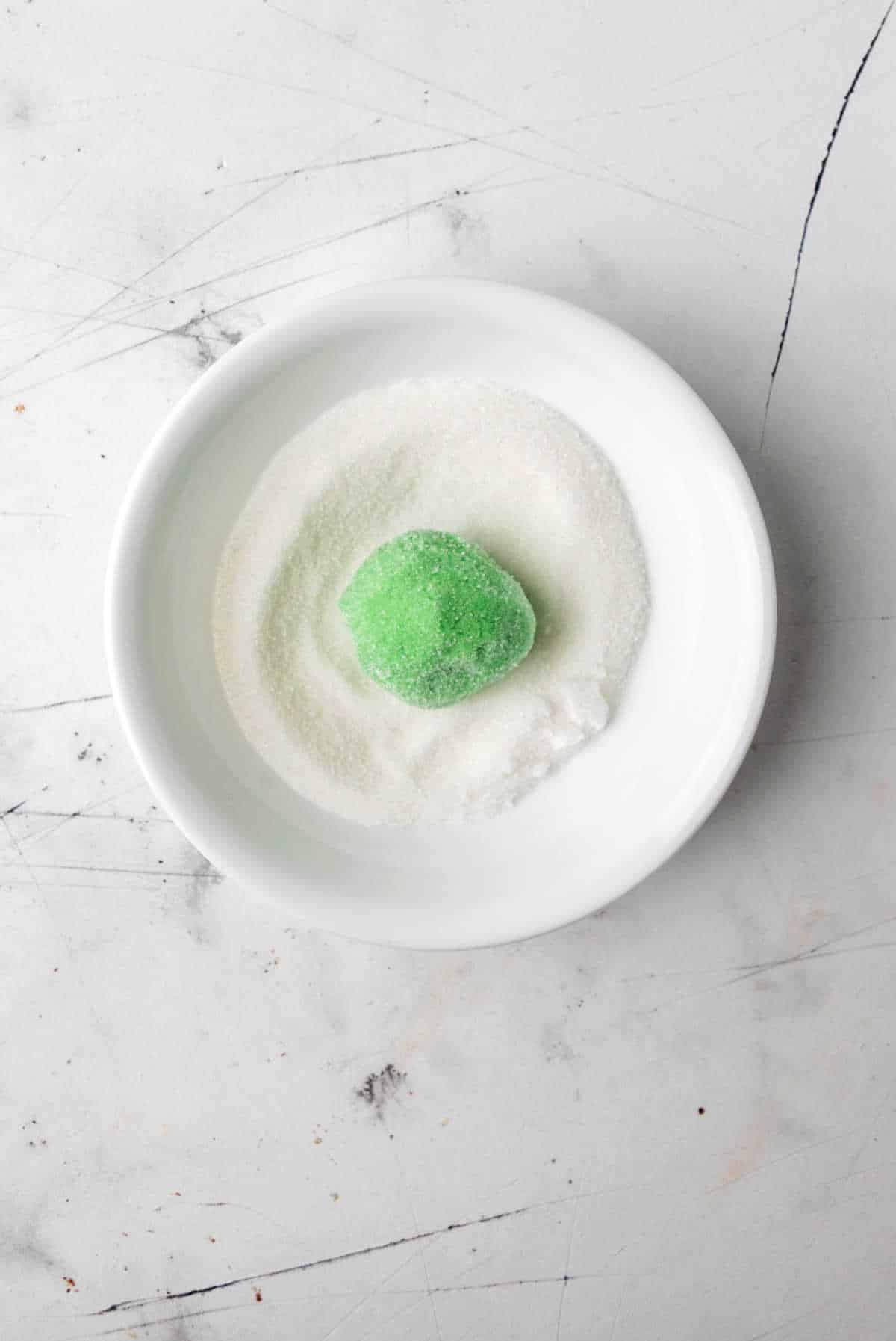 Scoop of Grinch cookie dough in dish of granulated sugar. 