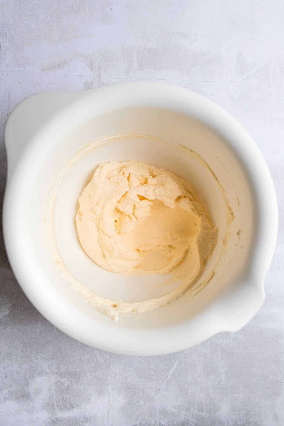 Beaten butter and cream cheese in a white mixing bowl. 