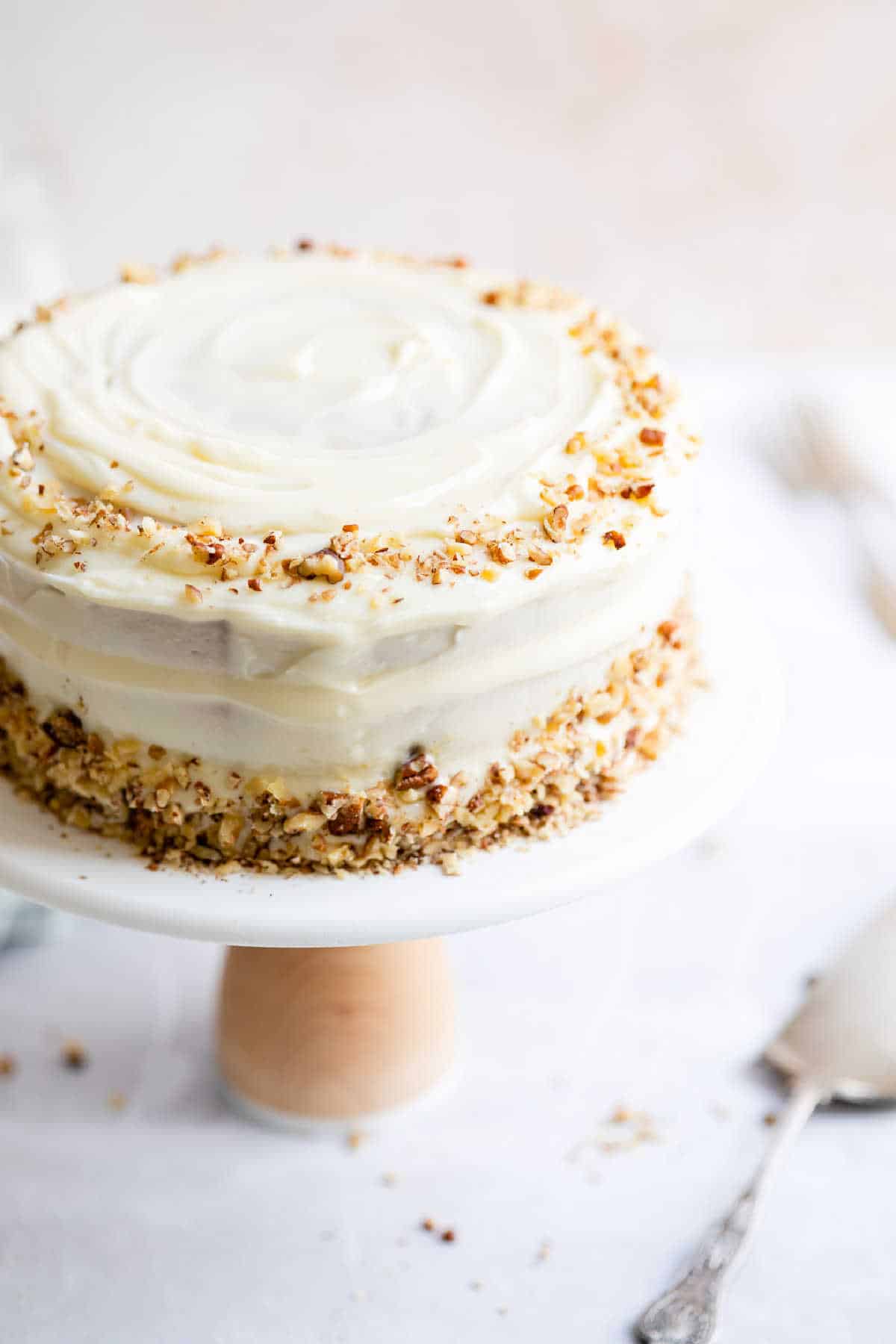 Italian cream cake on a white cake stand next to a cake server. 