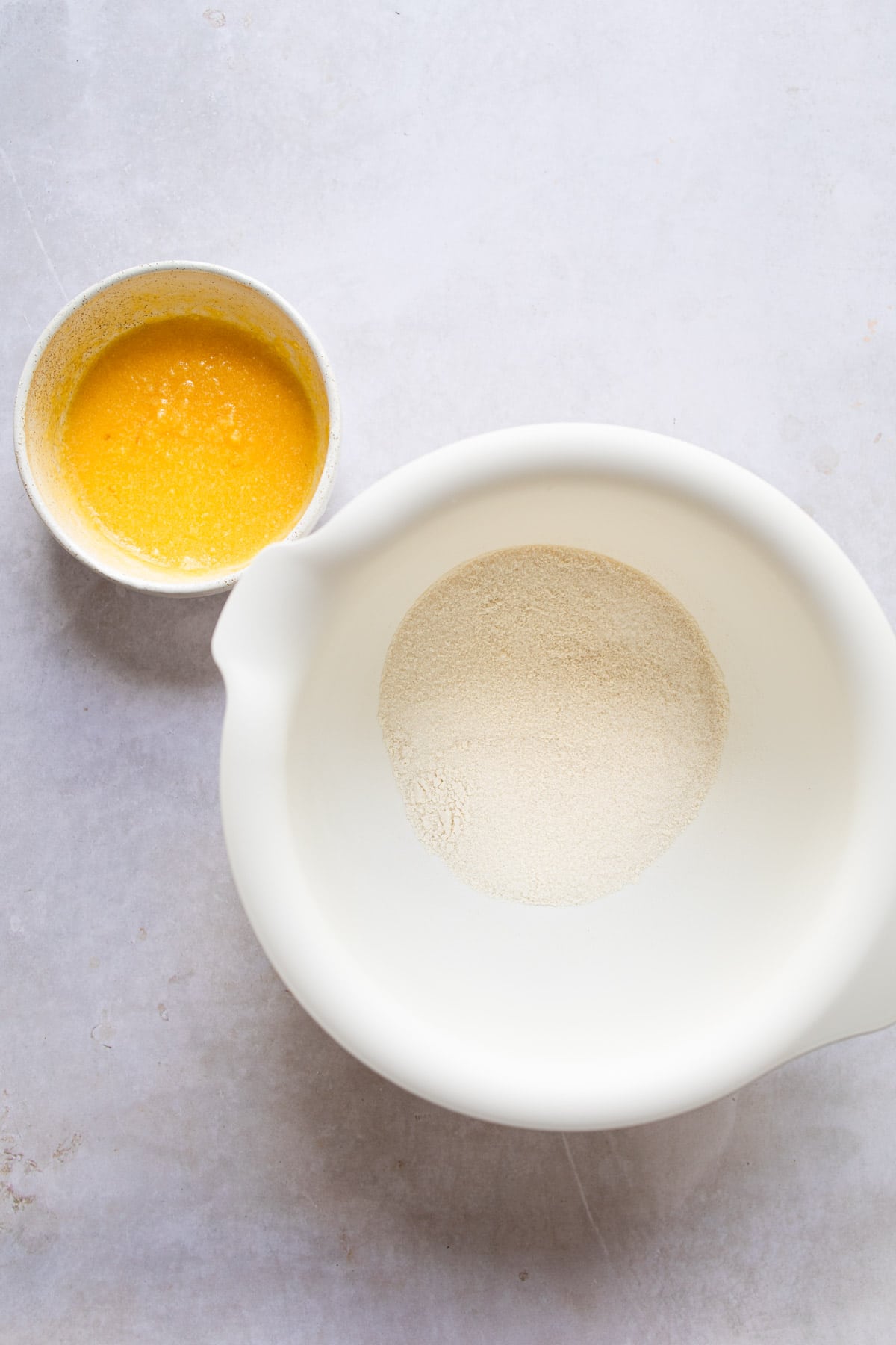 A white mixing bowl with flour and sugar in it. 