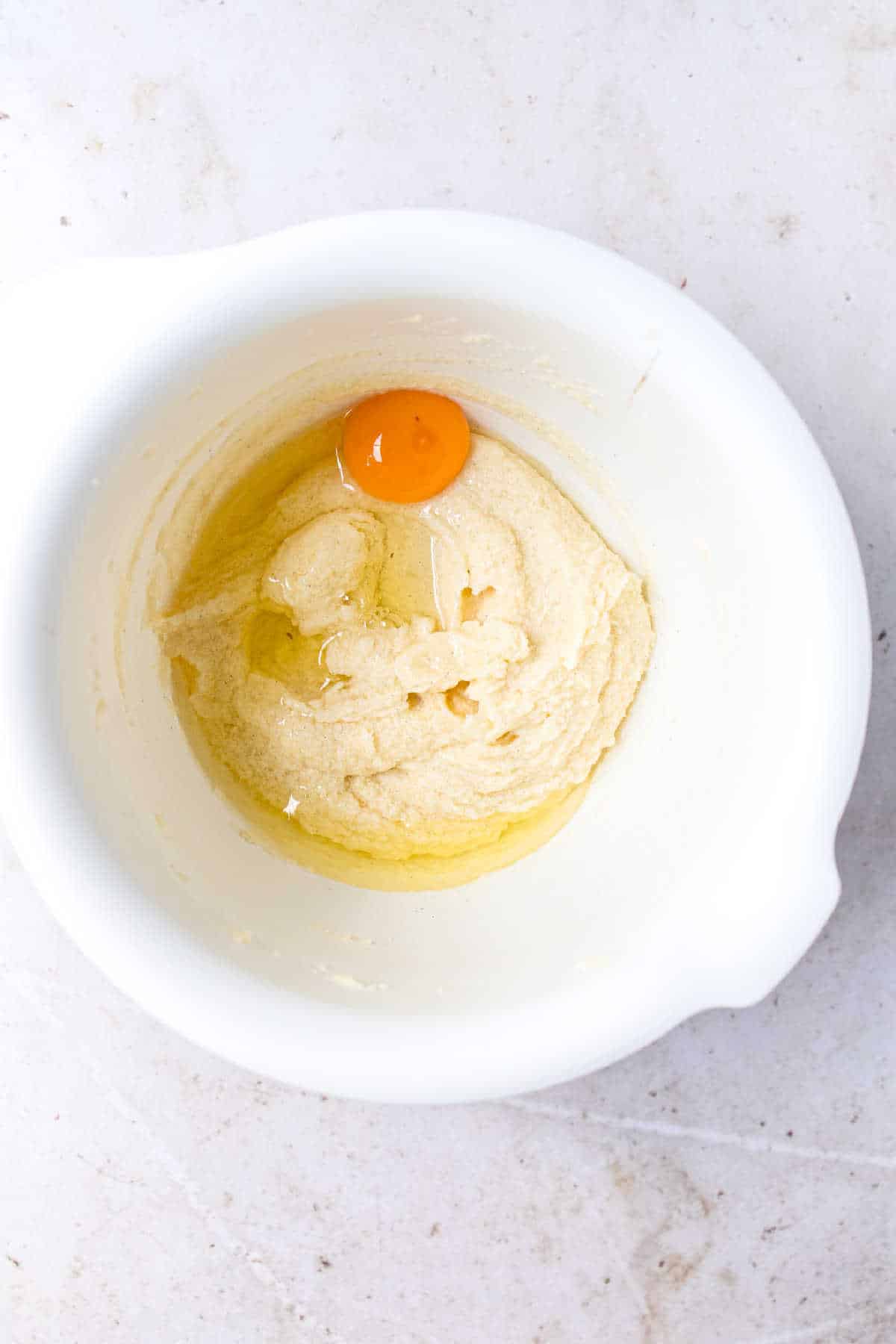 Egg on creamed butter and sugar in a white mixing bowl.