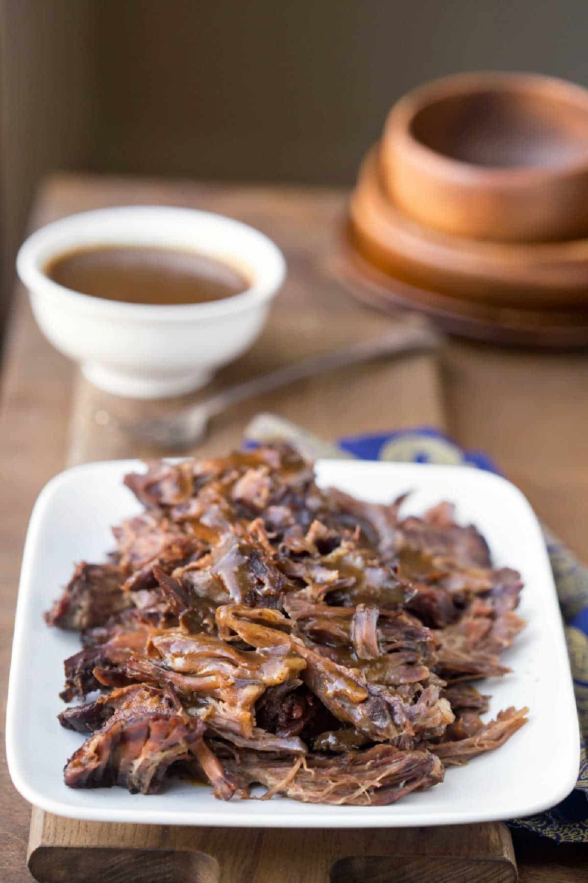 Crock Pot Balsamic Beef on a white platter next to a blue and yellow dish towel.