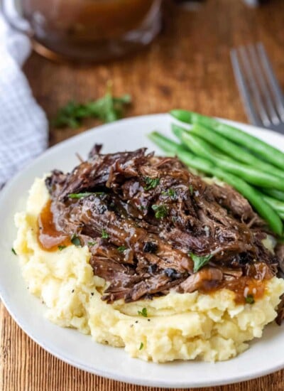 Crock pot balsamic beef on mashed potatoes next to green beans on a white plate.