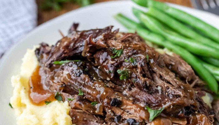 Crock pot balsamic beef on mashed potatoes next to green beans on a white plate.