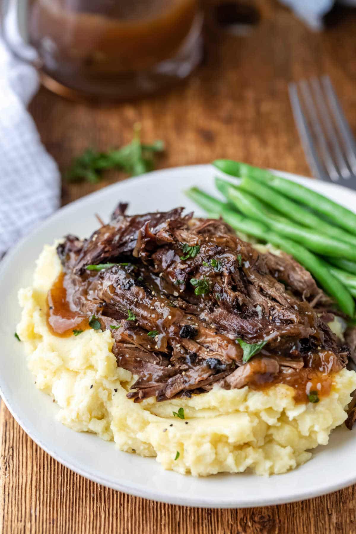 Crock pot balsamic beef on mashed potatoes next to green beans on a white plate. 