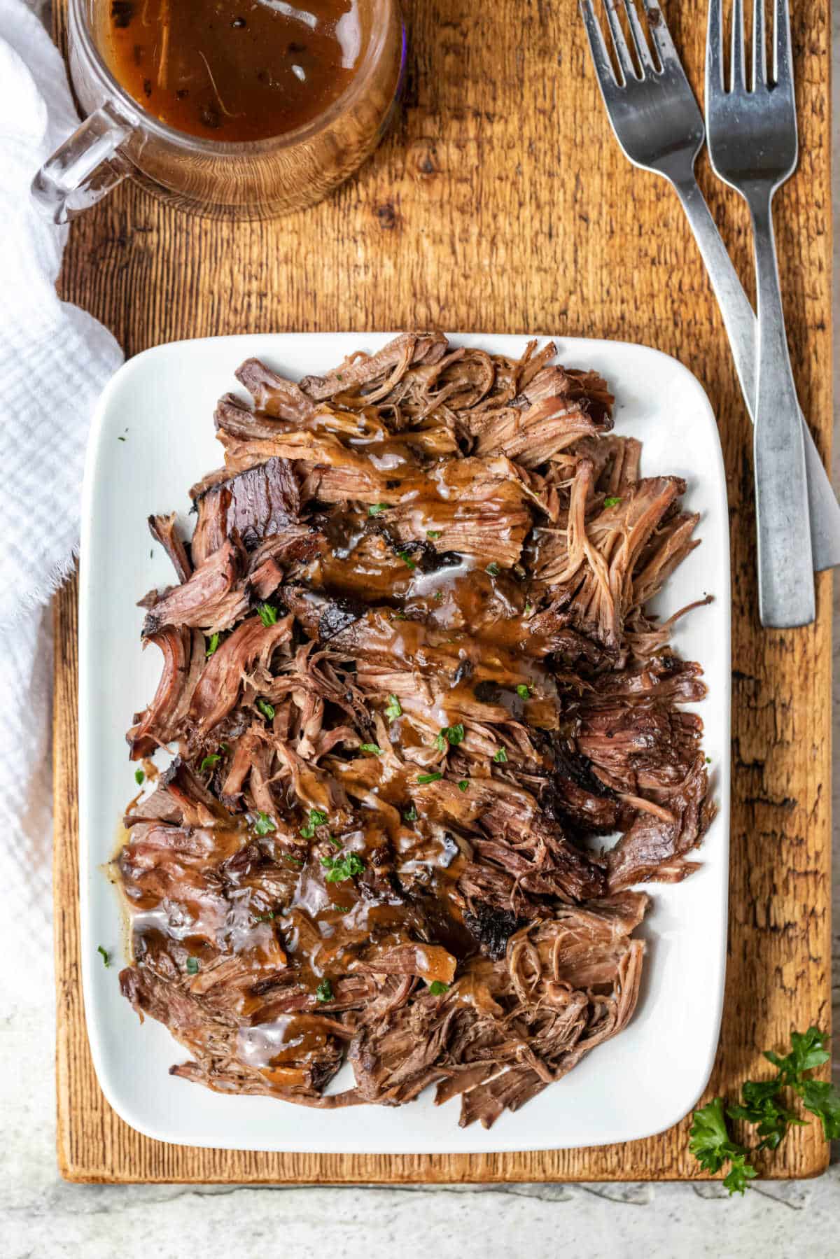 White platter full of balsamic beef next to two forks. 