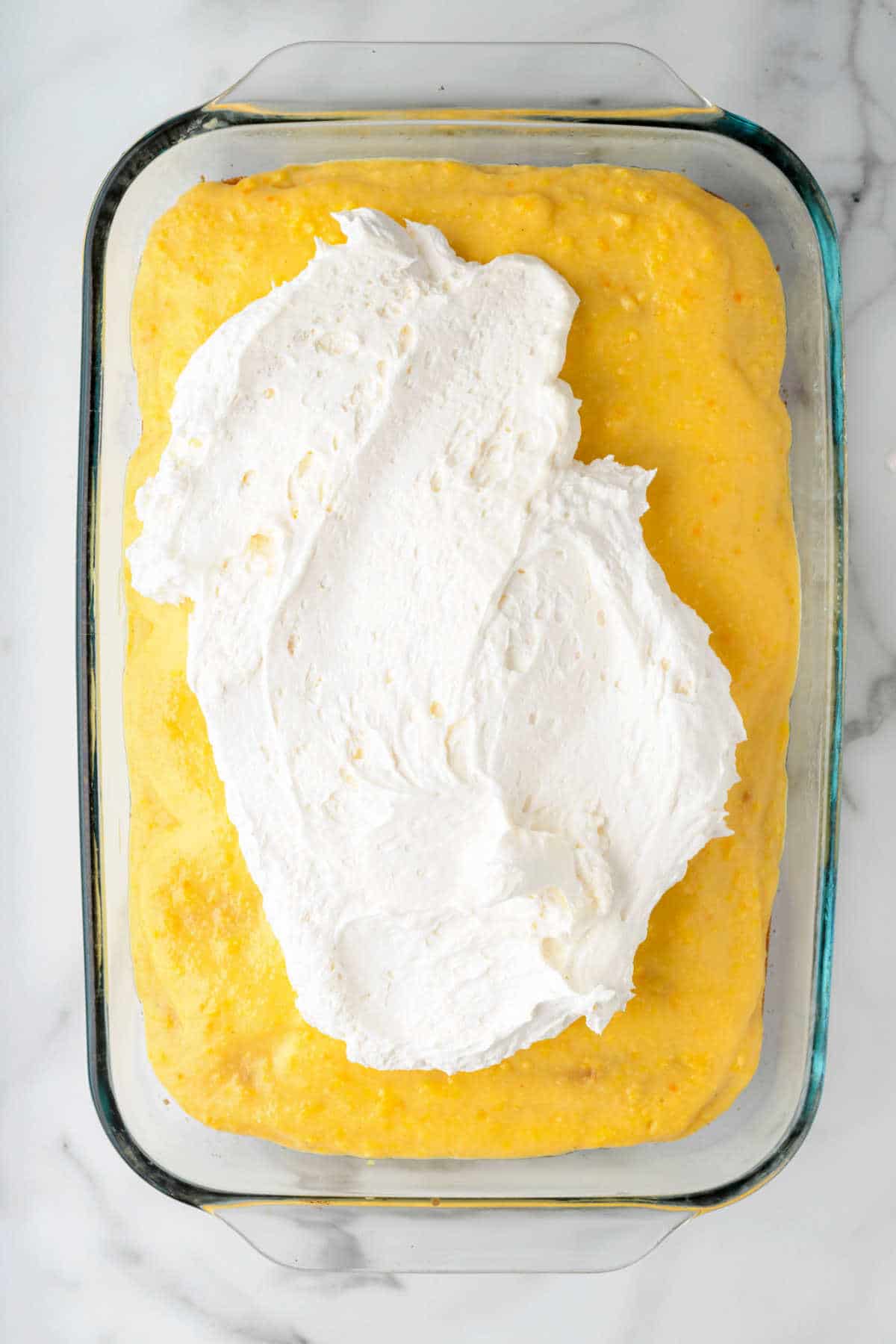 Cool whip being spread on a yellow cake.