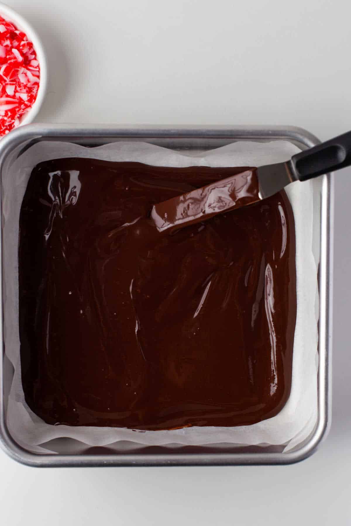 Offset spatula spreading chocolate in a baking pan.