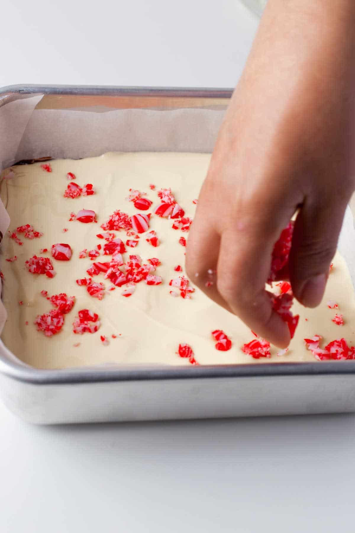 A hand sprinkling crushed candy canes over white chocolate. 