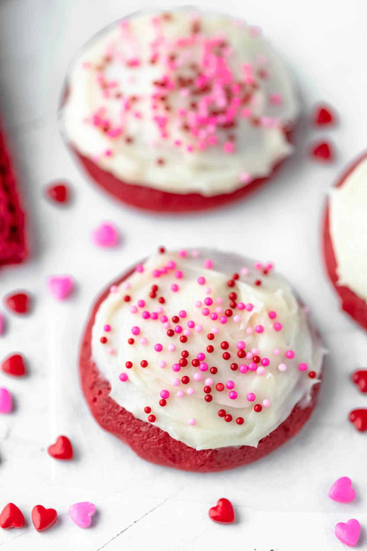 Two red velvet cookies topped with valentine's day sprinkles.