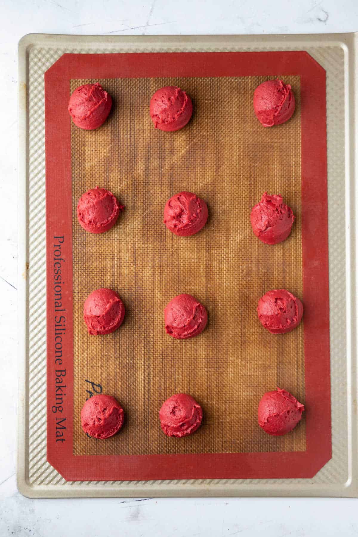 Scoops of red velvet cookie dough on a baking sheet. 