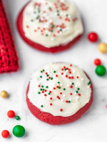 Two red velvet cookies next to colored sugar sprinkle balls.
