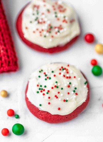 Two red velvet cookies next to colored sugar sprinkle balls.
